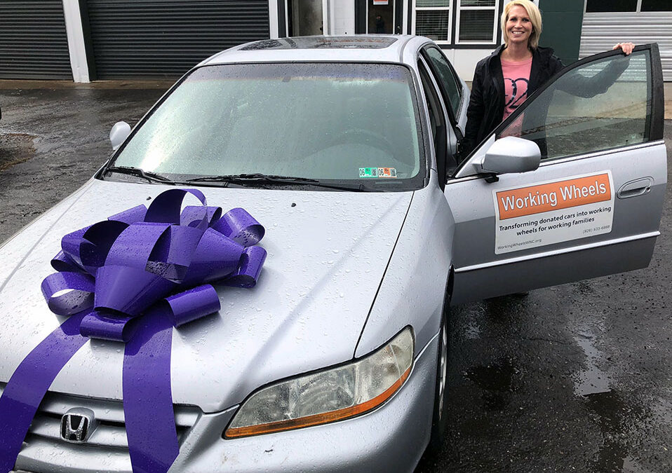 Woman standing next to her silver car with a purple bow on the hood