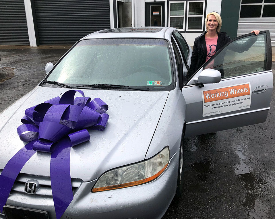 Woman standing next to her silver car with a purple bow on the hood